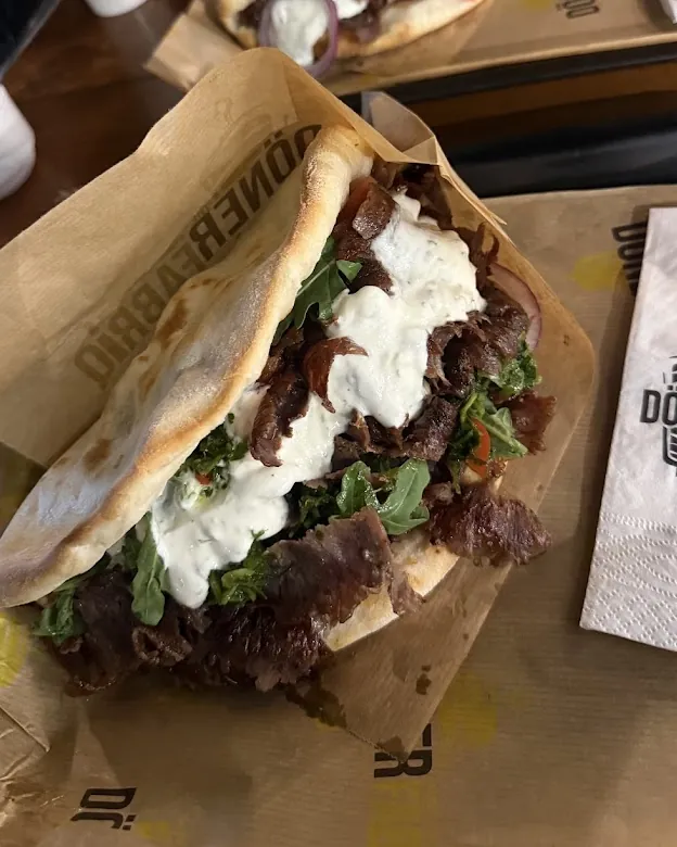 Zwei Döner mit weißer Soße auf dem Tablett, im Hintergrund Ayran