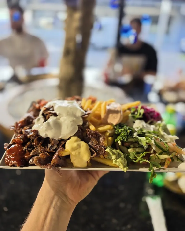 Ein Döner-Teller mit Pommes, Salat und mehreren Soßen wird auf der Hand gereicht